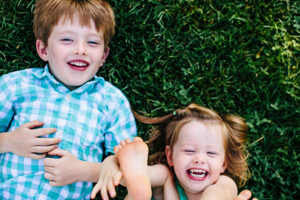 Children laugh and smile while wearing blue checkered shirts against green foliage.