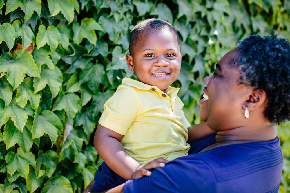 Parent and child share joyful moments against leafy green background.