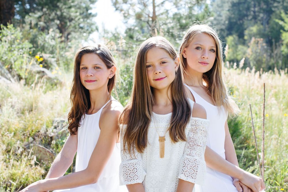 A group poses together outdoors wearing white dresses against a natural backdrop.