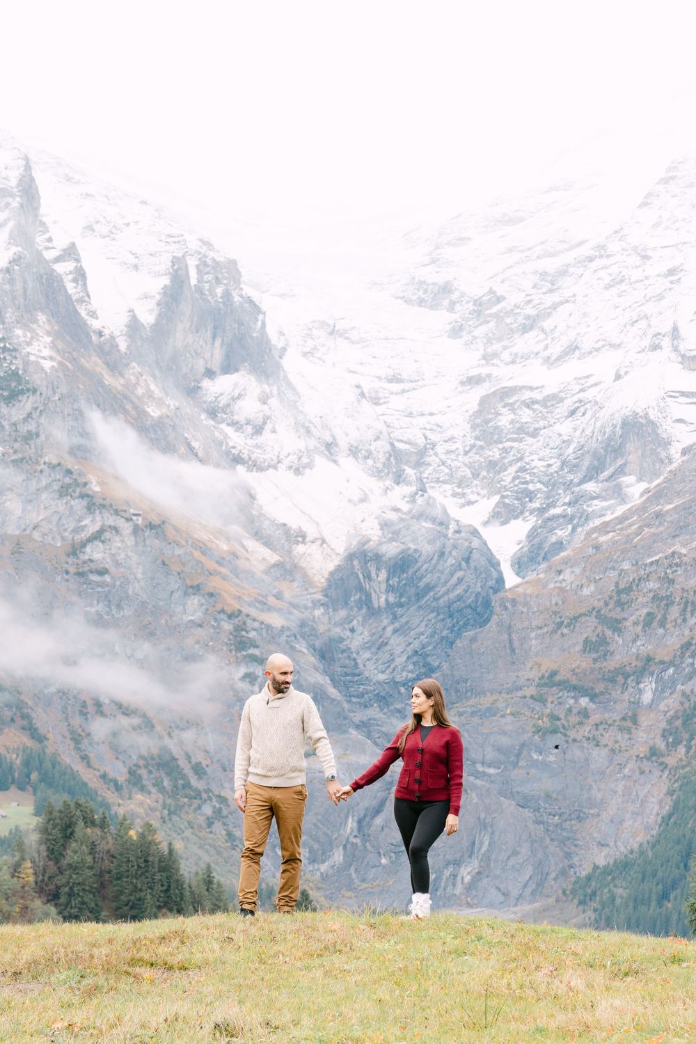 Couple playfully posing together on a grassy hillside with snow-capped Alps mountains in the background in Grindelwald.
