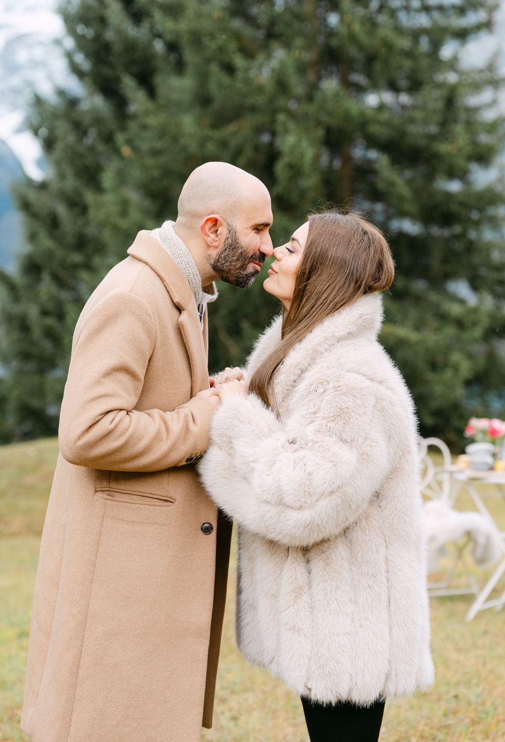 A couple shares a romantic moment outdoors in winter, with the person in beige coat embracing their partner in white fur.
