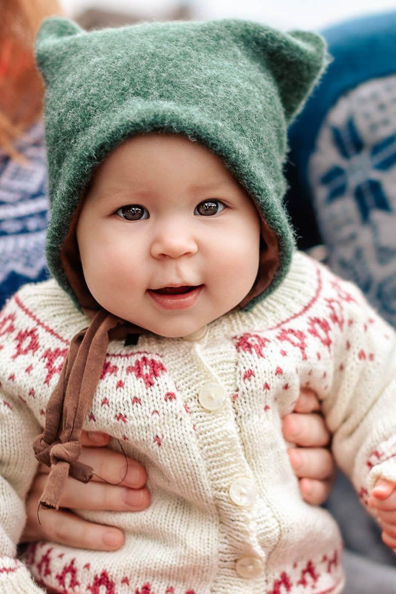 Baby med strikkegenser og grønn nisselue på.  Hun smiler til kamera.