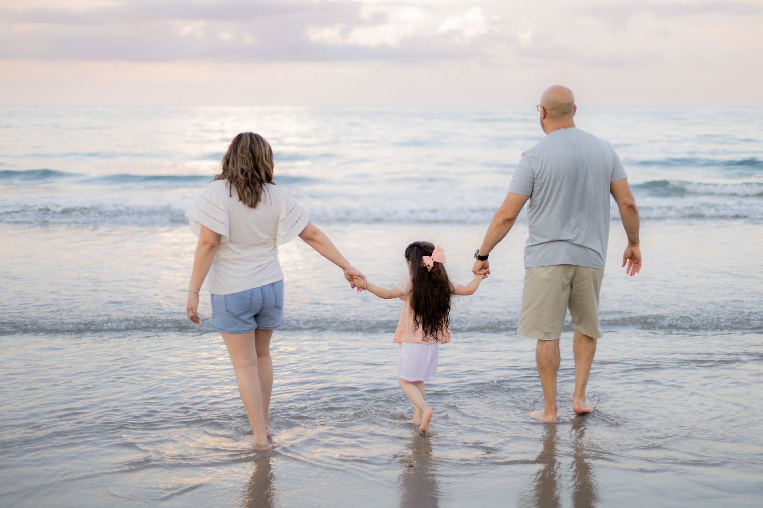 Family holding hands with feet in water looking out to ocean in Deerfield Beach