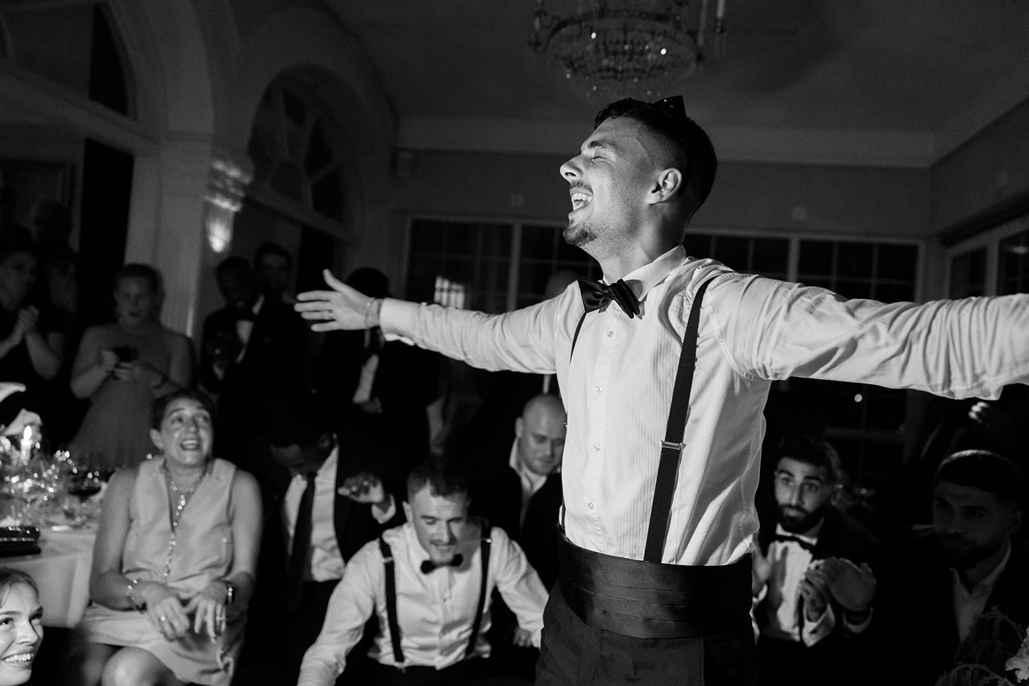 Wedding guests dance and celebrate together on a dimly lit dance floor at an evening reception.
