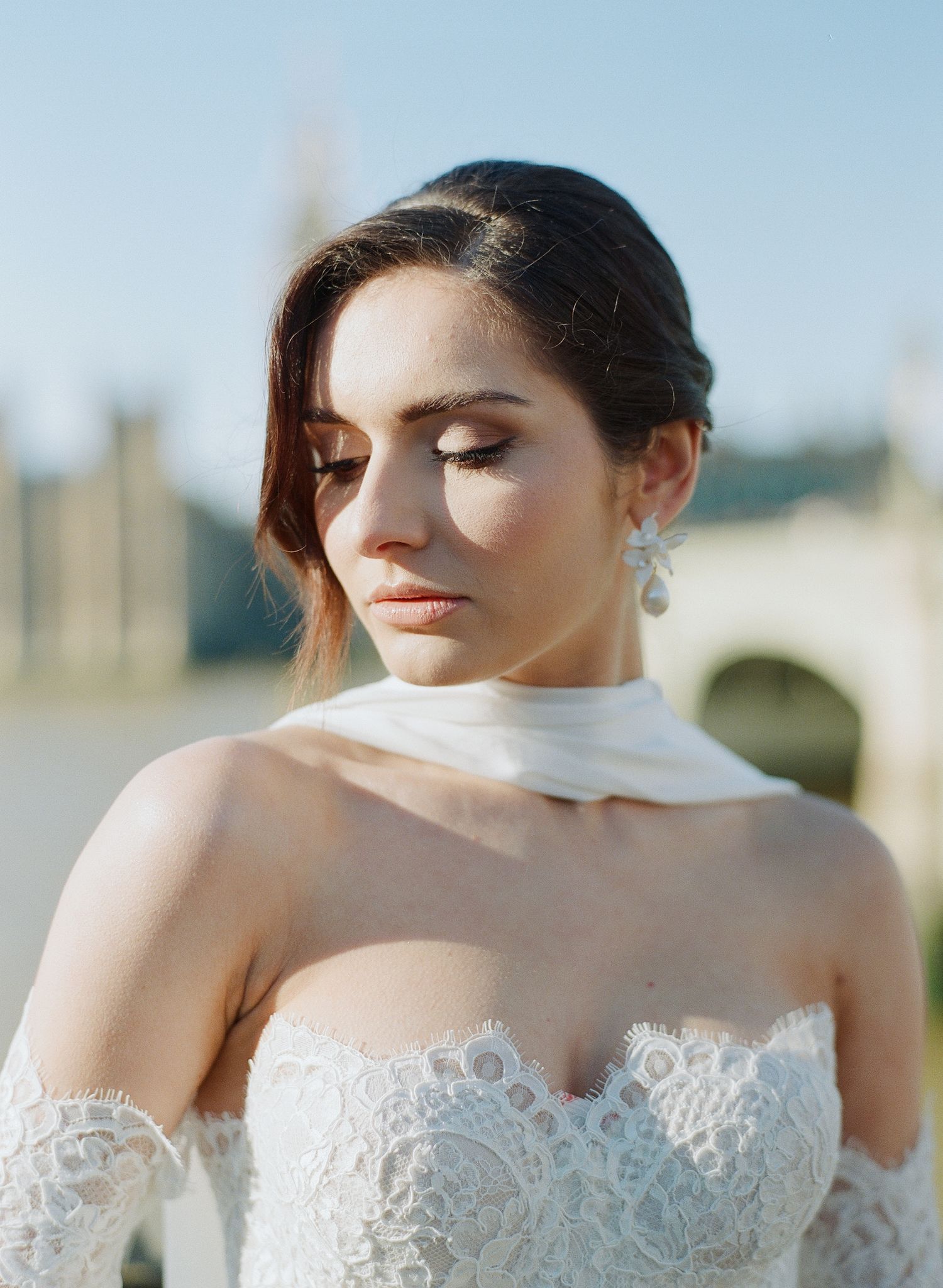 Close-up details of delicate white lace wedding dress bodice against blue sky.
