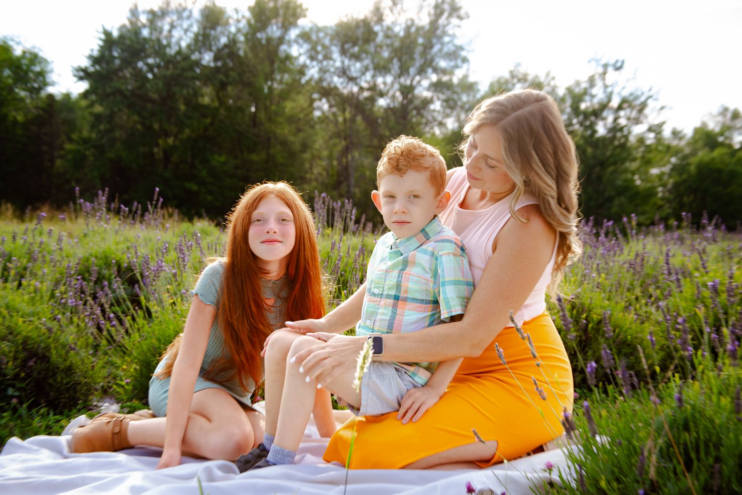 Three people sitting on blanket in field of purple wildflowers during golden hour.