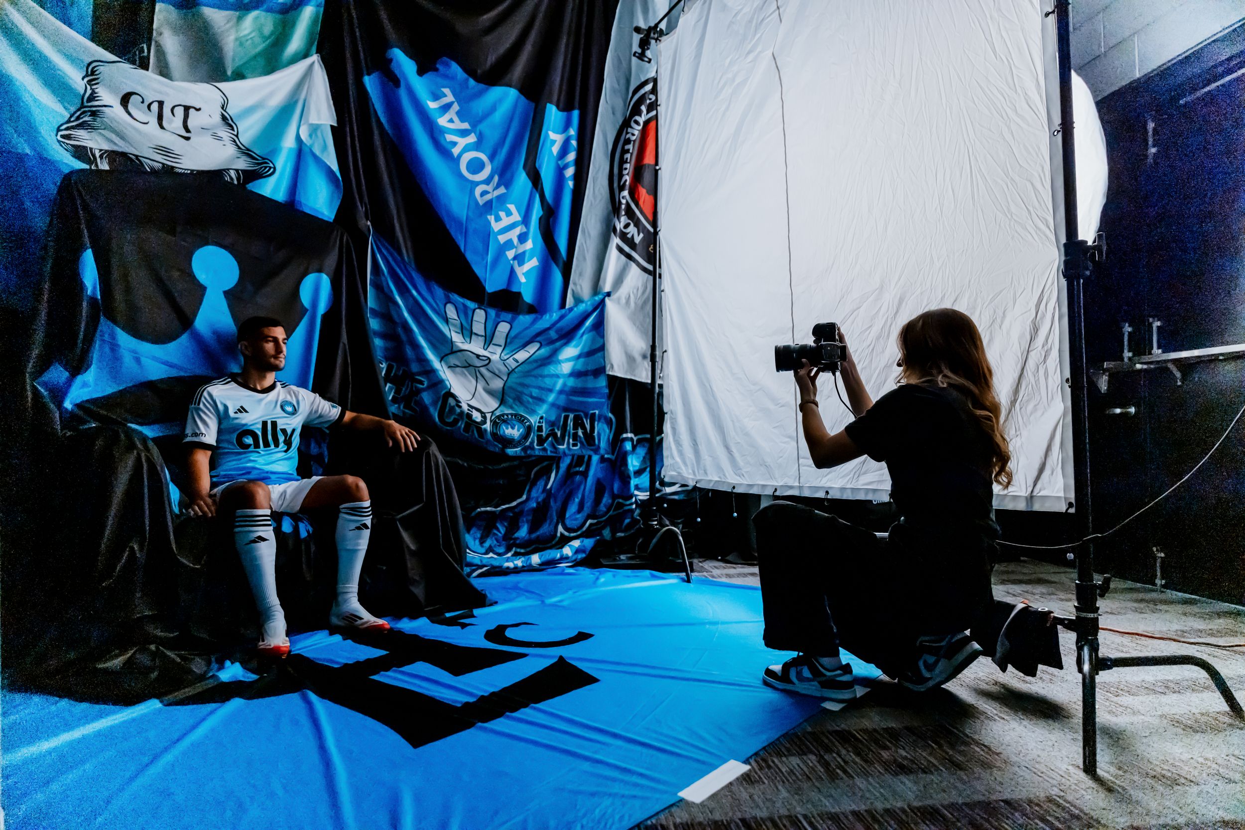 Charlotte FC player in white kit posed for professional photo shoot with photographer and team flags.