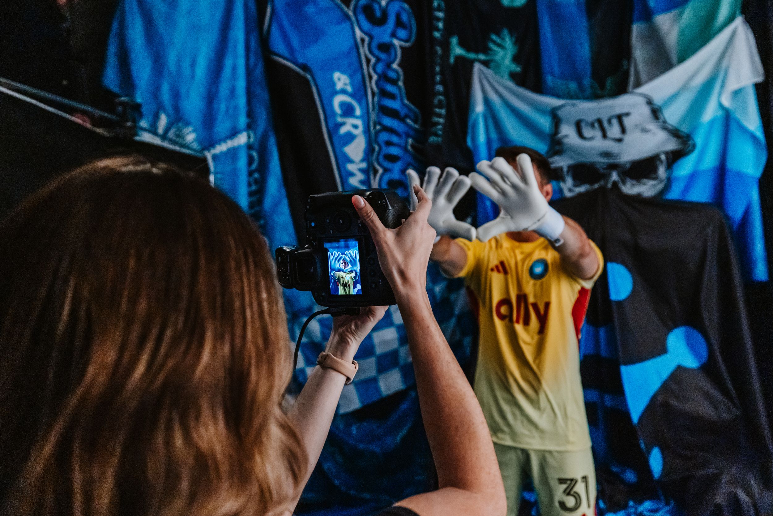 Photographer capturing Charlotte FC goalkeeper in yellow kit making crown hand gesture at photo shoot.