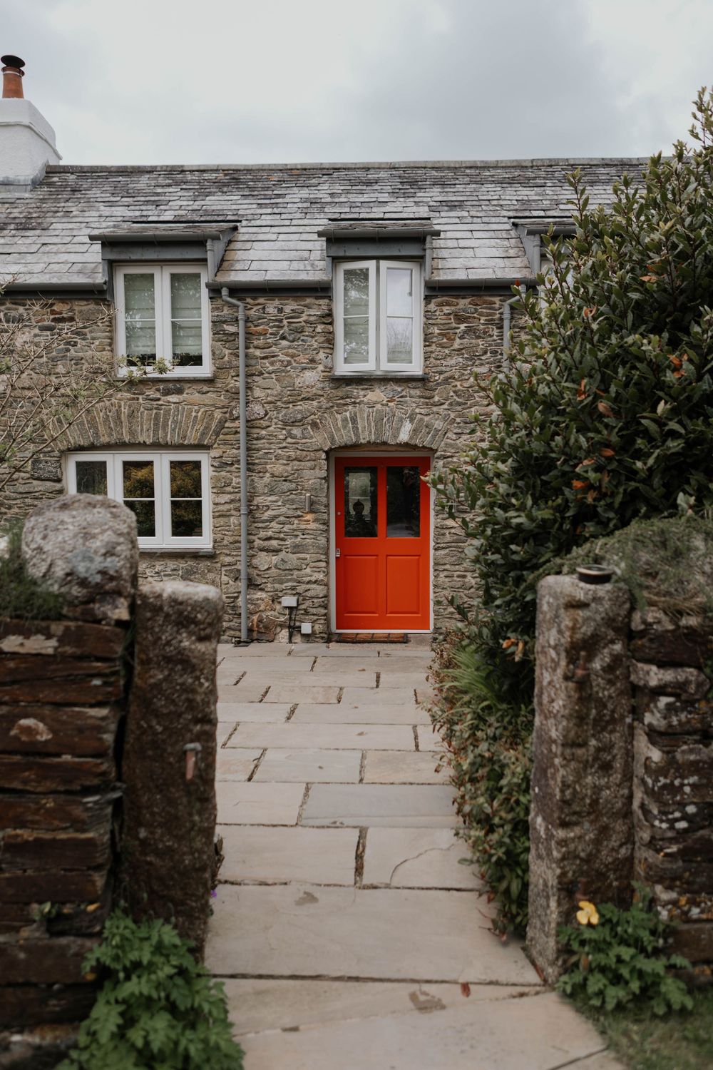 Charming stone cottage with vibrant red door and slate roof in countryside setting.