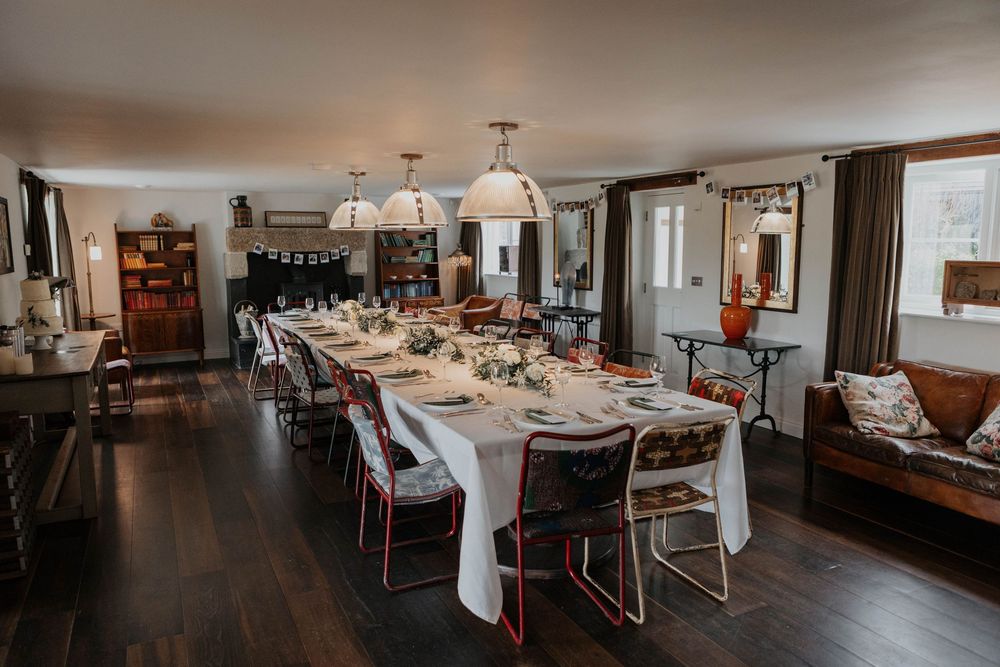Elegant long dining table set for wedding reception in rustic farmhouse interior.