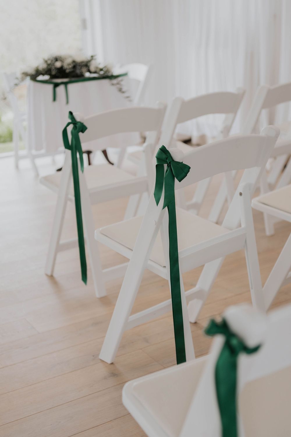 White folding chairs with elegant dark green ribbon bows at wedding ceremony venue.