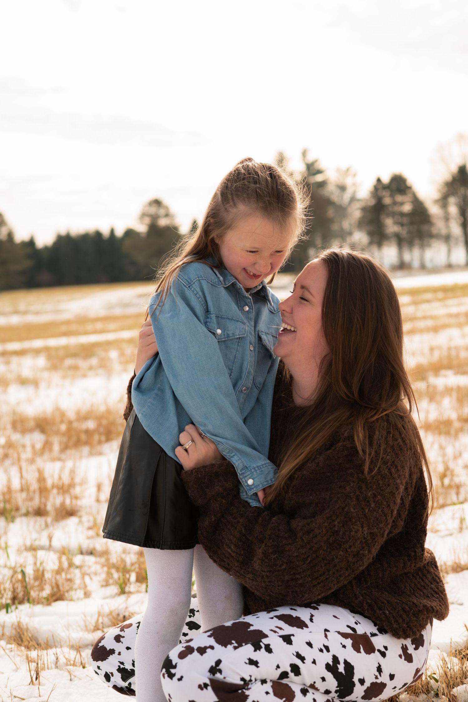 A parent and child share joyful moments together in a snowy winter field at sunset.