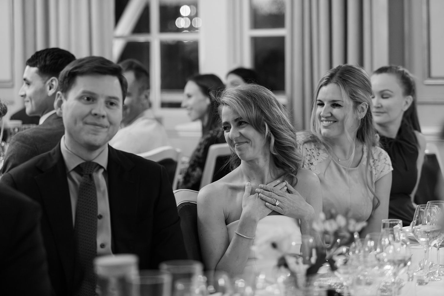 Black and white photo of wedding reception guests laughing and enjoying themselves at dining tables.