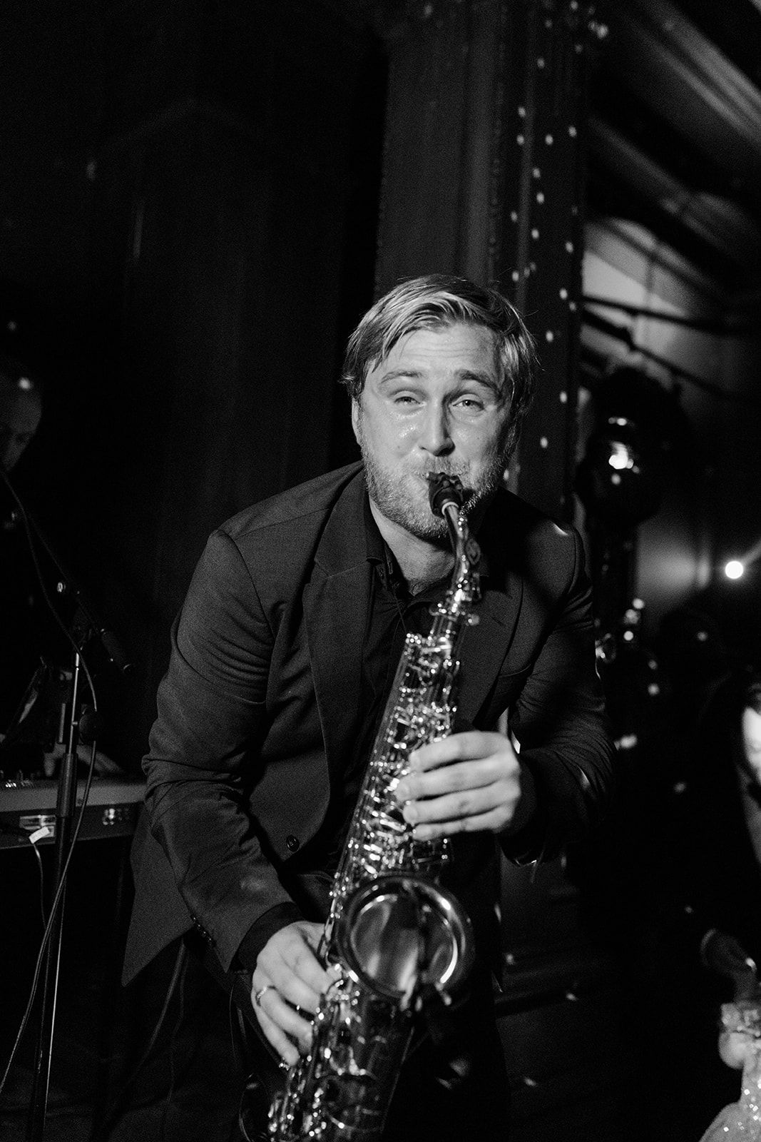 A musician plays a saxophone on stage in dramatic black and white lighting during a performance.