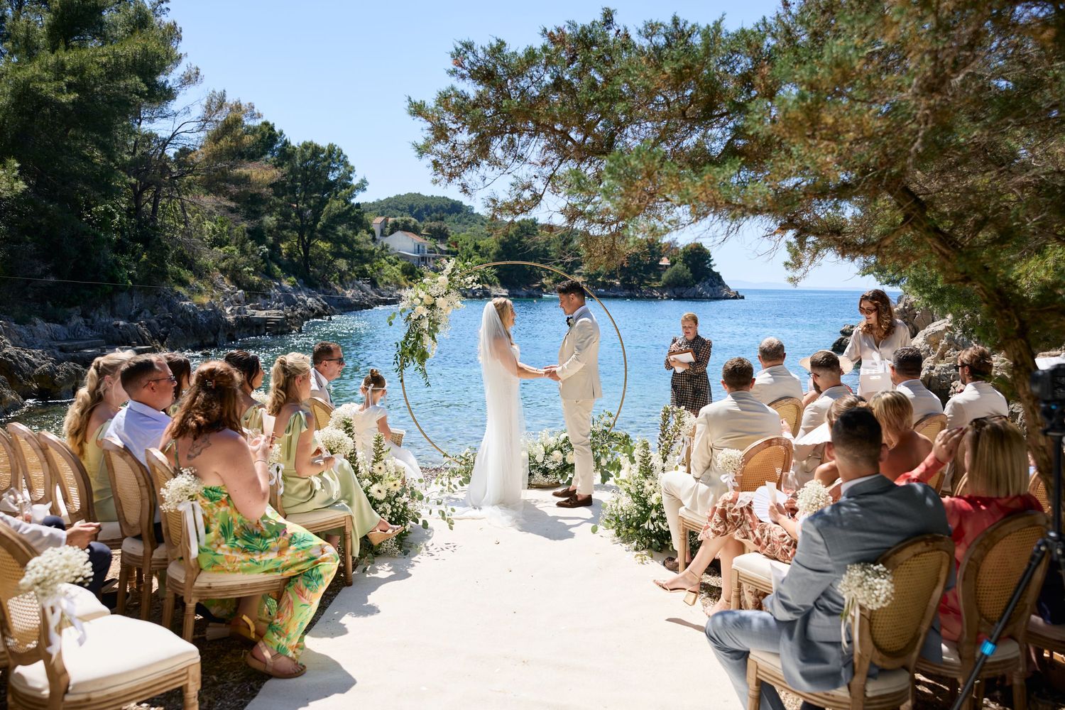 A scenic beach wedding ceremony setup with white chairs and floral arrangements on a tropical shoreline.