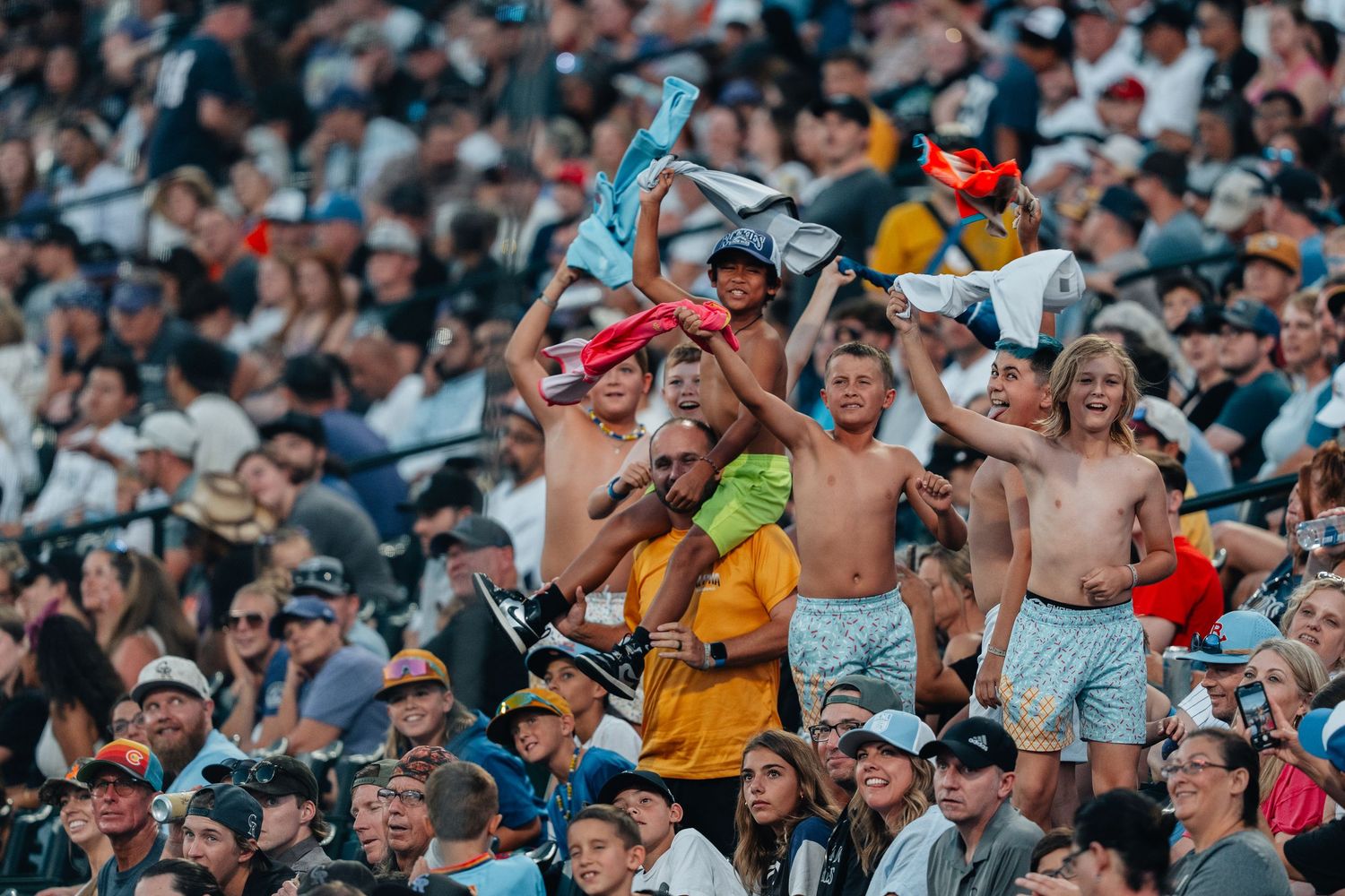 Large crowd of excited sports fans cheering and celebrating in stadium seating during a live event.