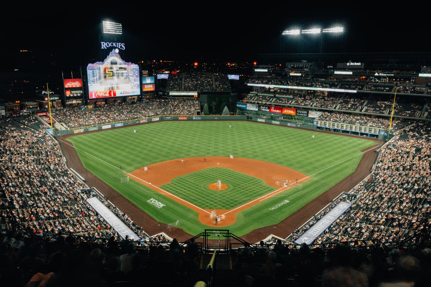 Panoramic view of a baseball stadium during a night game showing the illuminated field and filled grandstands.
