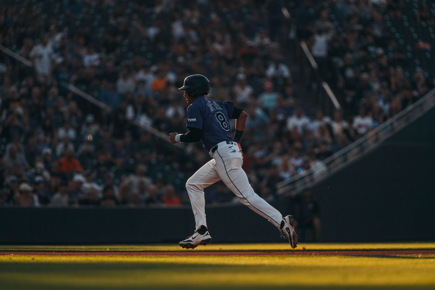 Baseball player in white uniform slides into base during night game as fielder attempts to make the tag.