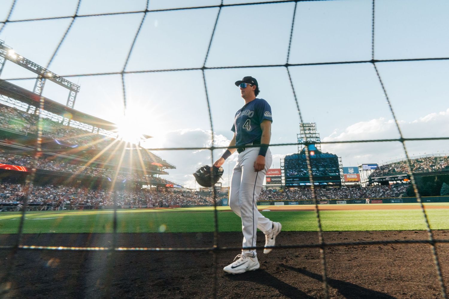 Baseball players stand on a field during a game with stadium lights and netting visible in the background.