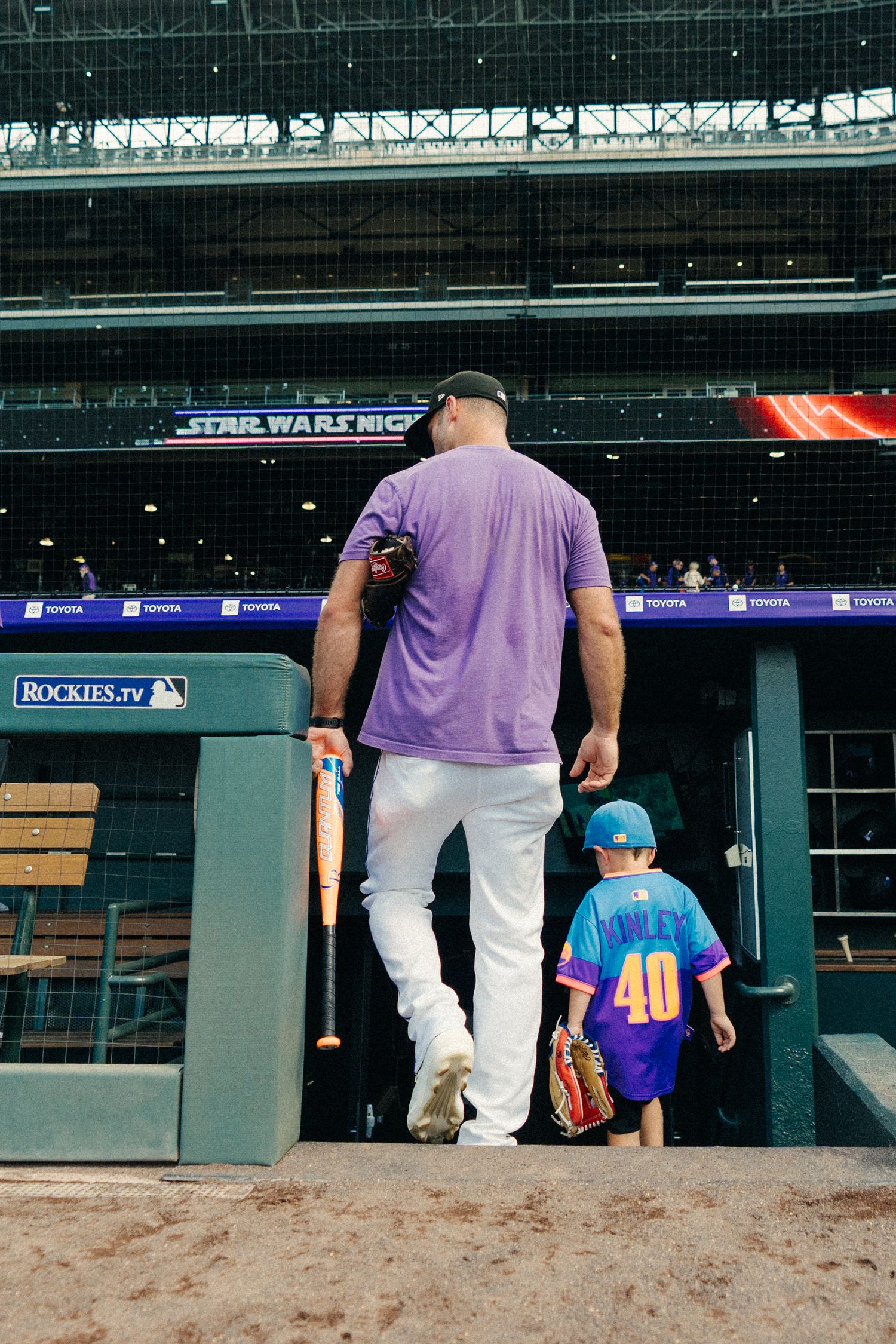 An adult and child in baseball uniforms walk together through a stadium tunnel at a baseball game.