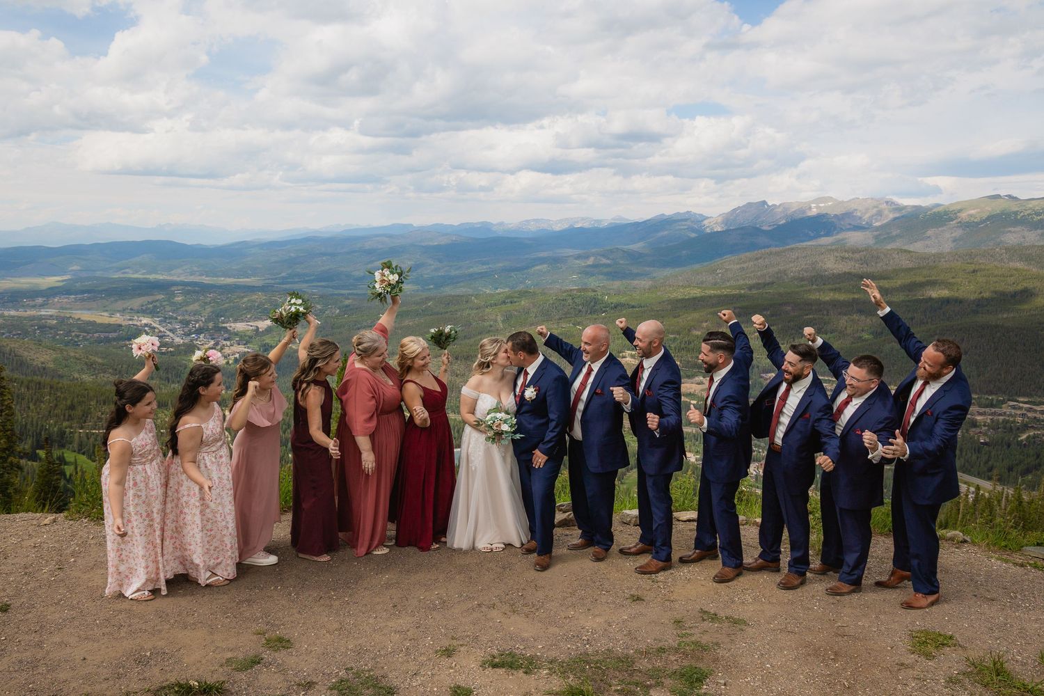 Wedding party stands in line against scenic mountain backdrop with dramatic cloudy sky in Colorado.
