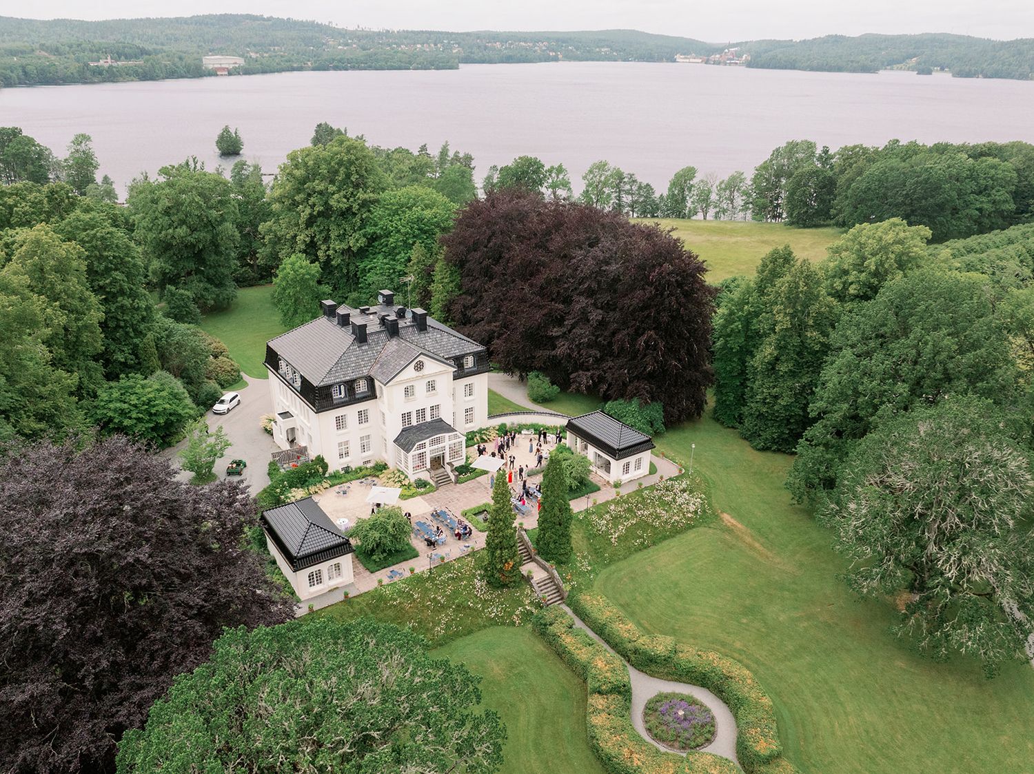 Aerial view of elegant white houses with manicured lawns nestled along a tranquil waterfront setting.