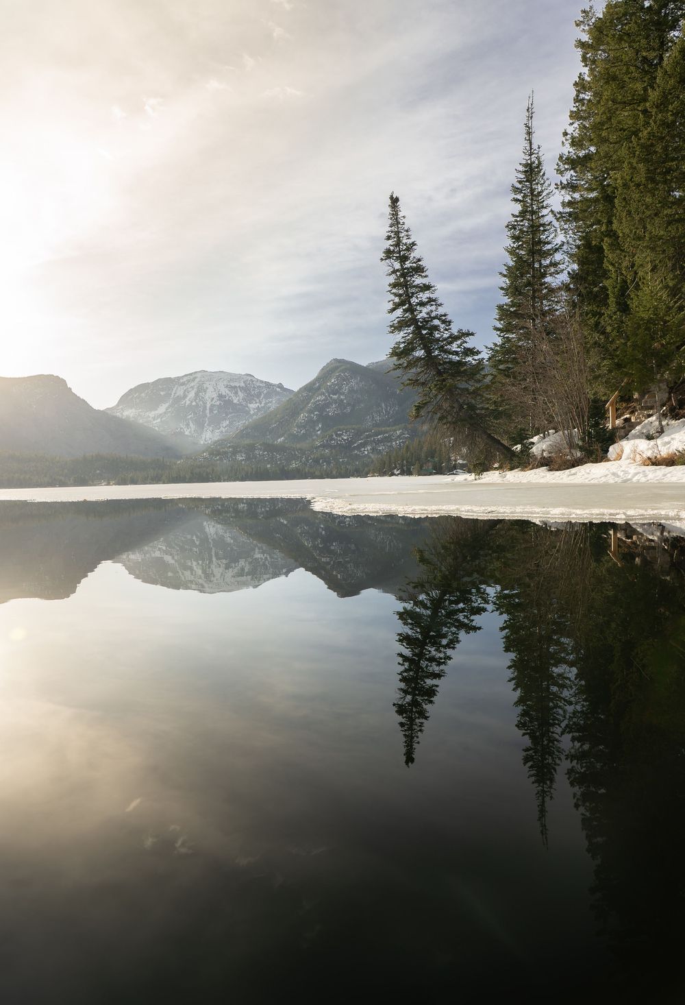 Serene mountain lake surrounded by snow-capped peaks and evergreen trees reflecting in calm waters at dusk.