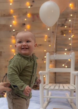 Festive first birthday setup with white rocking chair and balloon decorations.