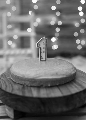 Black and white photo of a birthday cake with number 1 candle on top against bokeh lights.