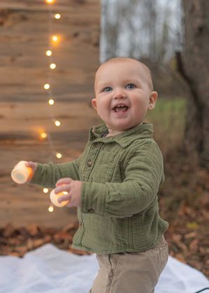 A sequence of a baby in green clothing playing outdoors with twinkle lights in the background.