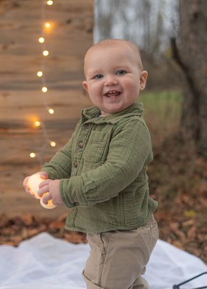 Green shirt and khaki pants outfit against rustic backdrop with string lights.