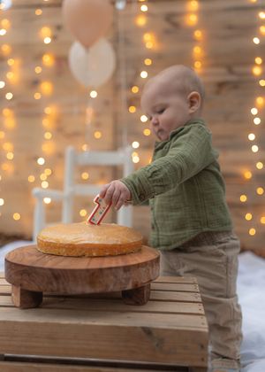 A first birthday celebration setup with a cake on wooden stand and twinkle lights in background.