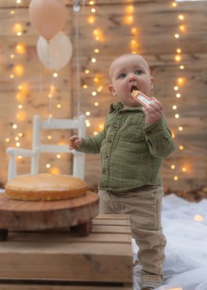 A series showing a baby in olive green clothing playing in a winter setting with string lights.