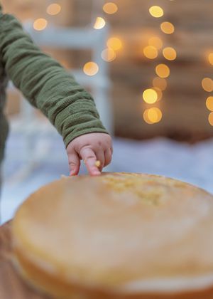 Close up of small hand reaching for birthday cake with golden bokeh lights in background.