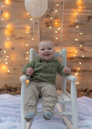 White rocking chair and balloon setup for first birthday photoshoot with twinkle lights.