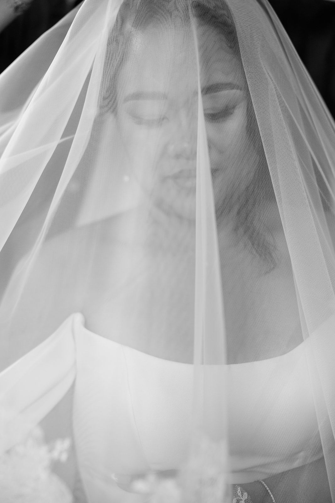 A serene black and white portrait of a bride wearing a delicate veil that softly drapes over her face.