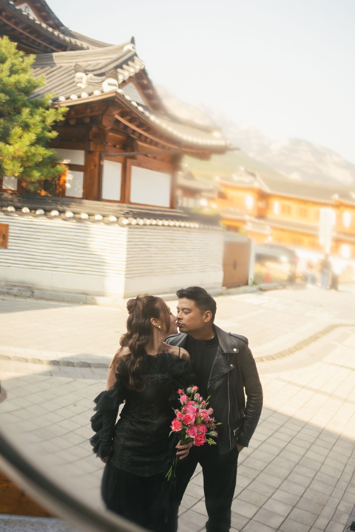 A couple in black outfits shares romantic moments at a traditional Korean temple complex during sunset.