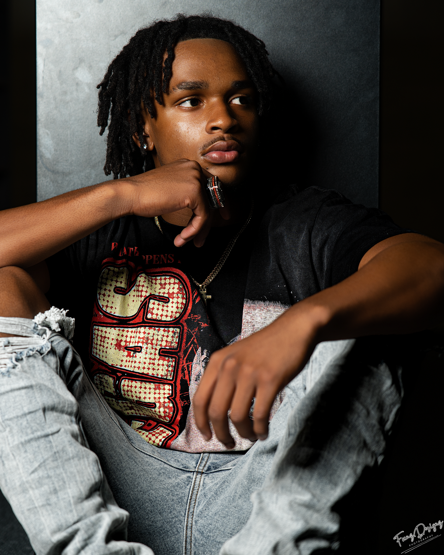 Artistic portrait in moody lighting shows subject wearing vintage t-shirt and distressed denim against dark background.