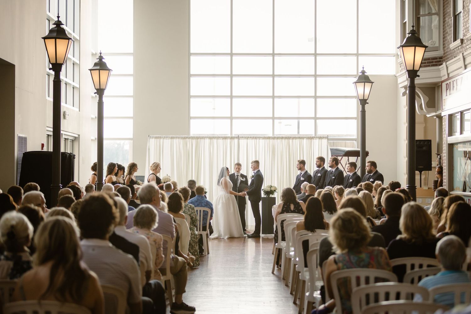 Wedding guests seated in rows during an elegant ceremony with lantern-style lighting fixtures along the walls.