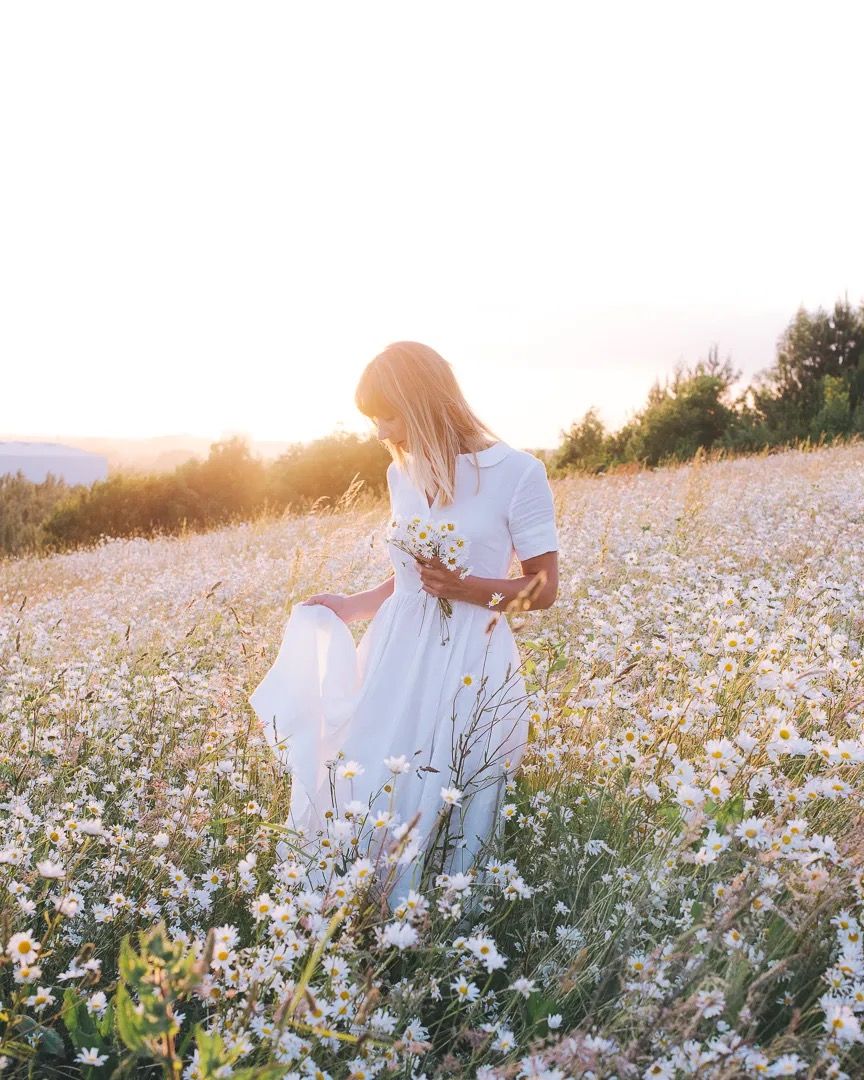 Woman in a white dress walking through a wildflower field at sunset.