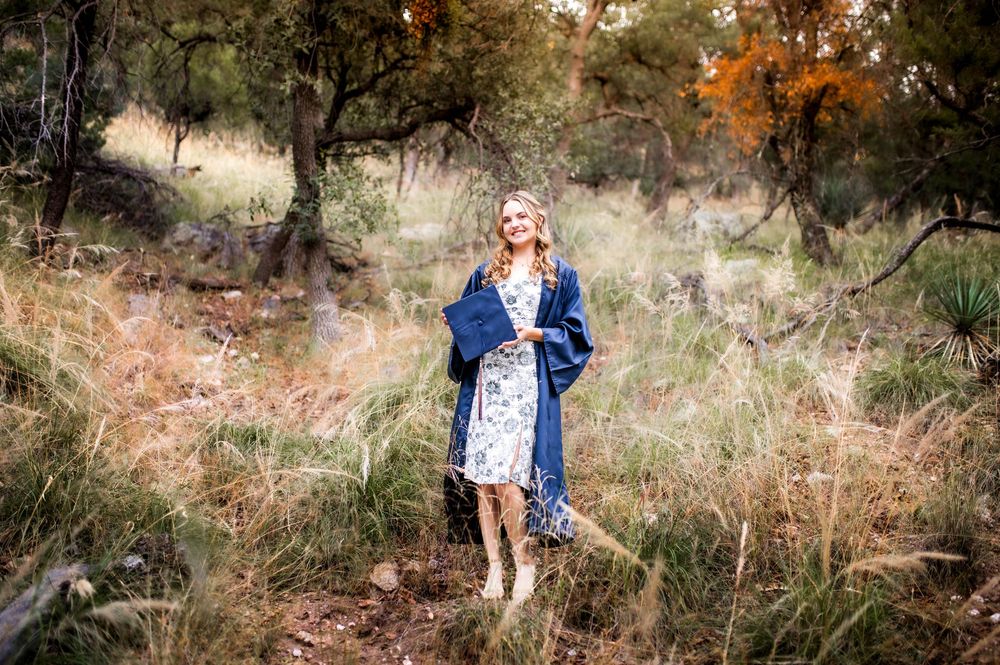 Young woman in floral dress and blue kimono walking through a wooded meadow.