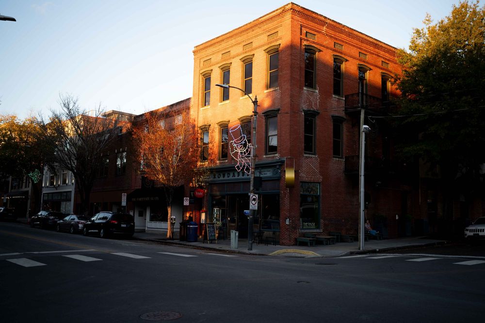 Historic brick buildings line a quiet street corner in a downtown district at sunset with warm golden lighting.