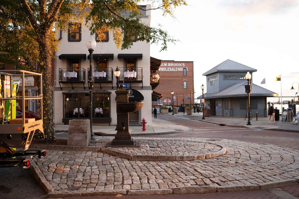 Historic cobblestone street corner in downtown district with brick buildings and lamp posts at dusk.