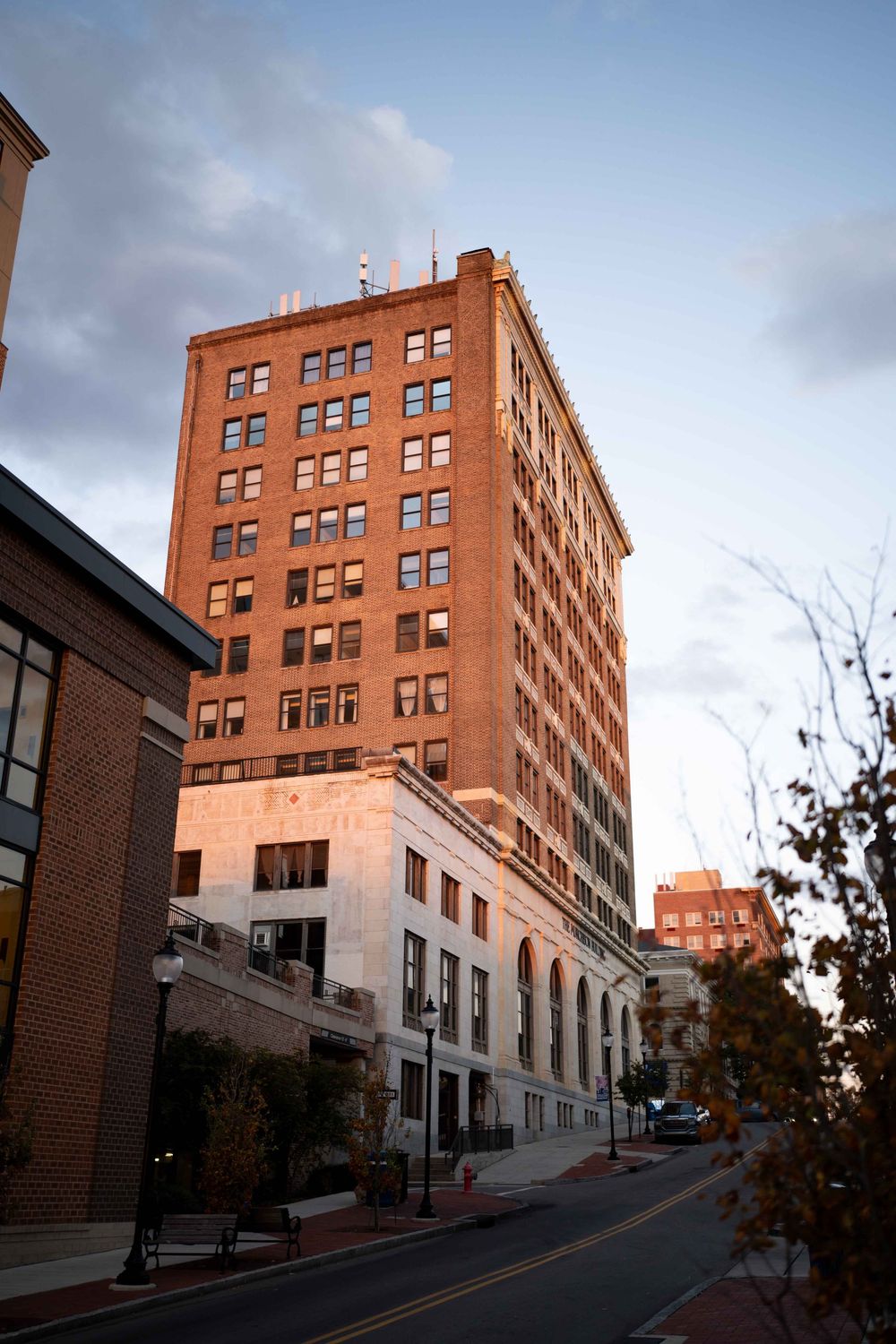 Tall brick office building with terracotta facade stands against cloudy sky on sloping city street at dusk.