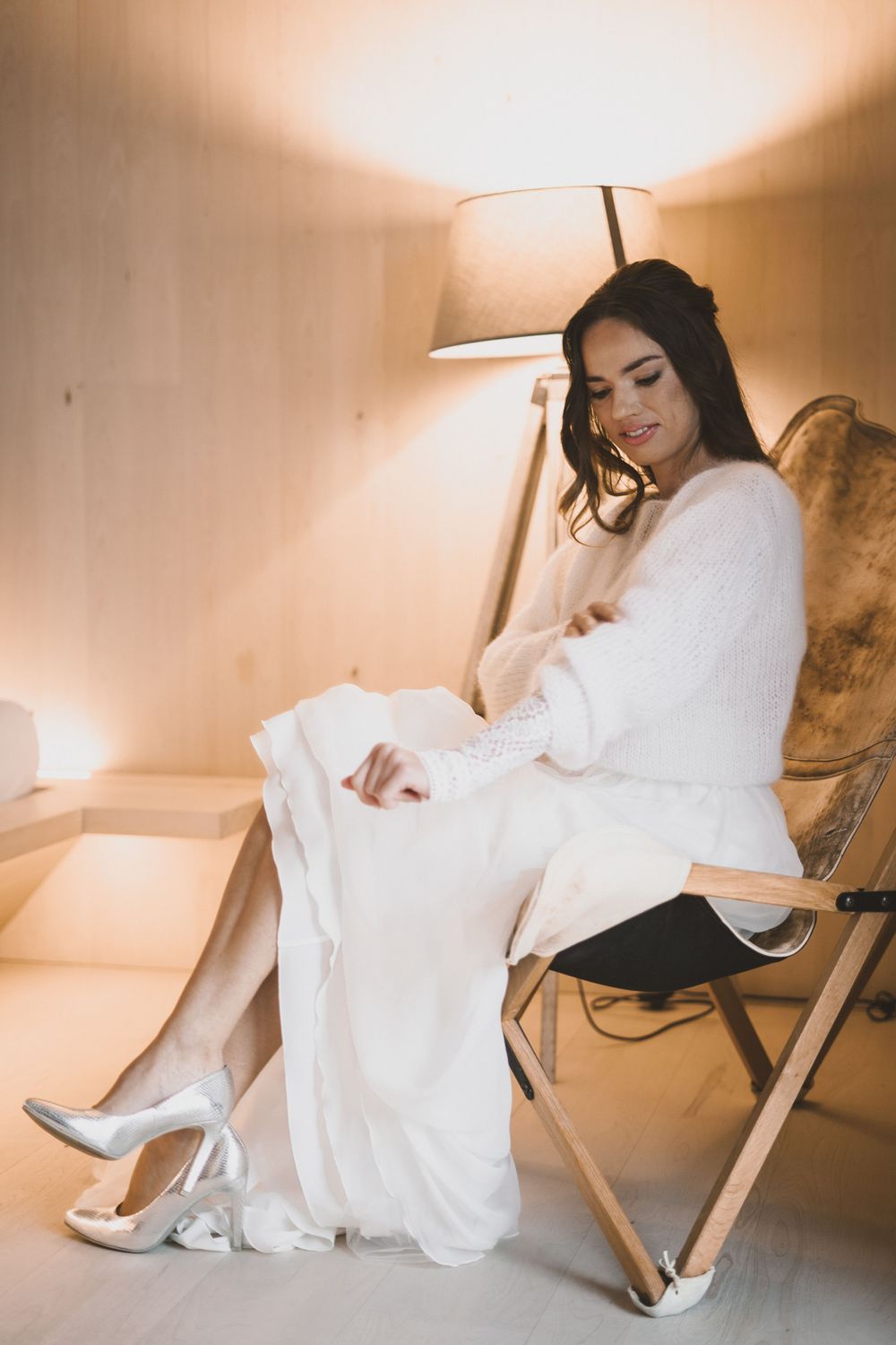 Elegant bridal photoshoot featuring a white dress and heels in a warmly lit indoor setting.