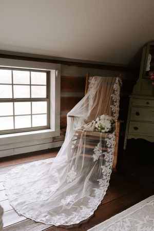 Delicate lace wedding veil spread across wooden floor near window light.