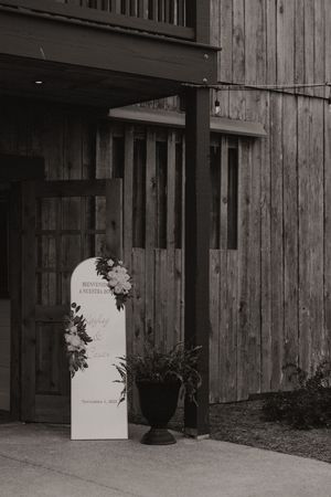 Rustic wooden building entrance with white signage and potted plants against weathered wood siding.