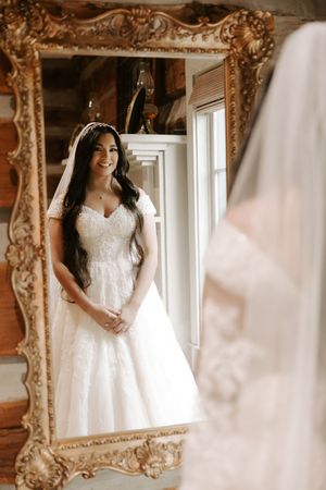 A reflection in an ornate gold mirror shows a wedding dress in a rustic cabin setting.