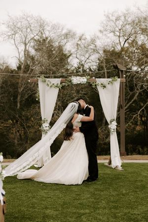 Romantic outdoor wedding ceremony setup with flowing white fabric draped between wooden posts.