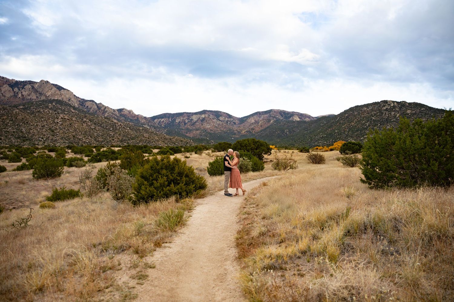 A scenic hiking trail winds through rugged desert terrain with mountains visible in the distance.